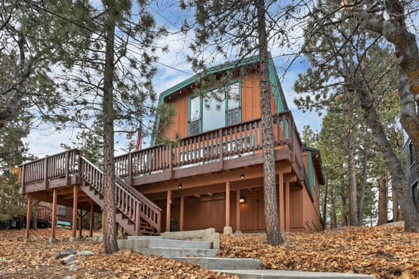 A two-story cabin with a wooden deck and stairs leading to a balcony.