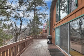 A wooden deck with a grill and an American flag, overlooking a forested area.