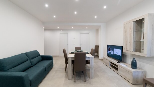Een moderne woonkamer met een bank, een eettafel, stoelen, een televisie en een kast.
