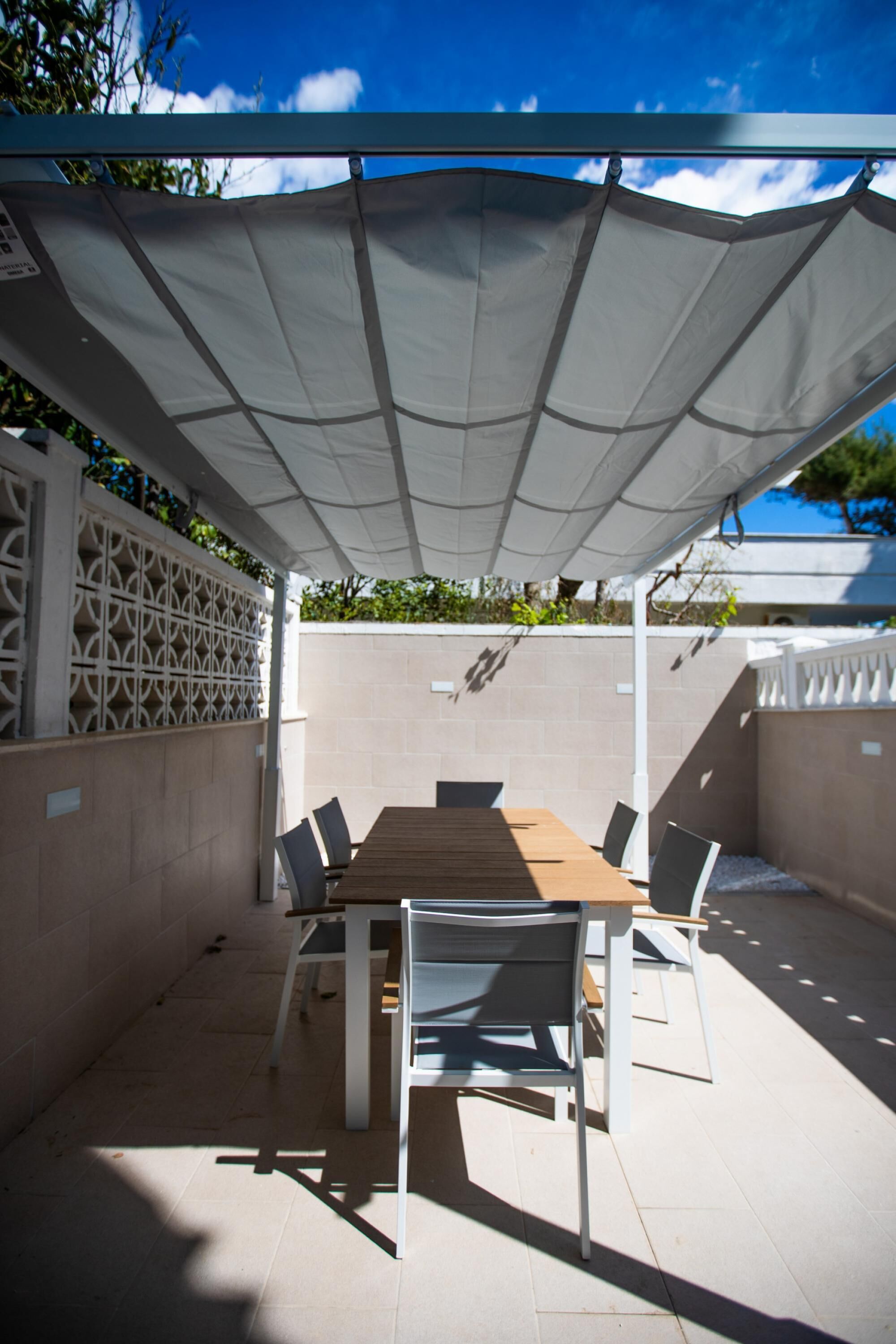 Une terrasse extérieure avec une table et des chaises en bois, un auvent blanc et un sol carrelé.