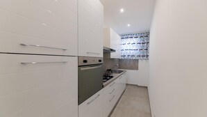 Een moderne keuken met witte kasten, roestvrijstalen apparatuur en een raam met gordijnen met een patroon.