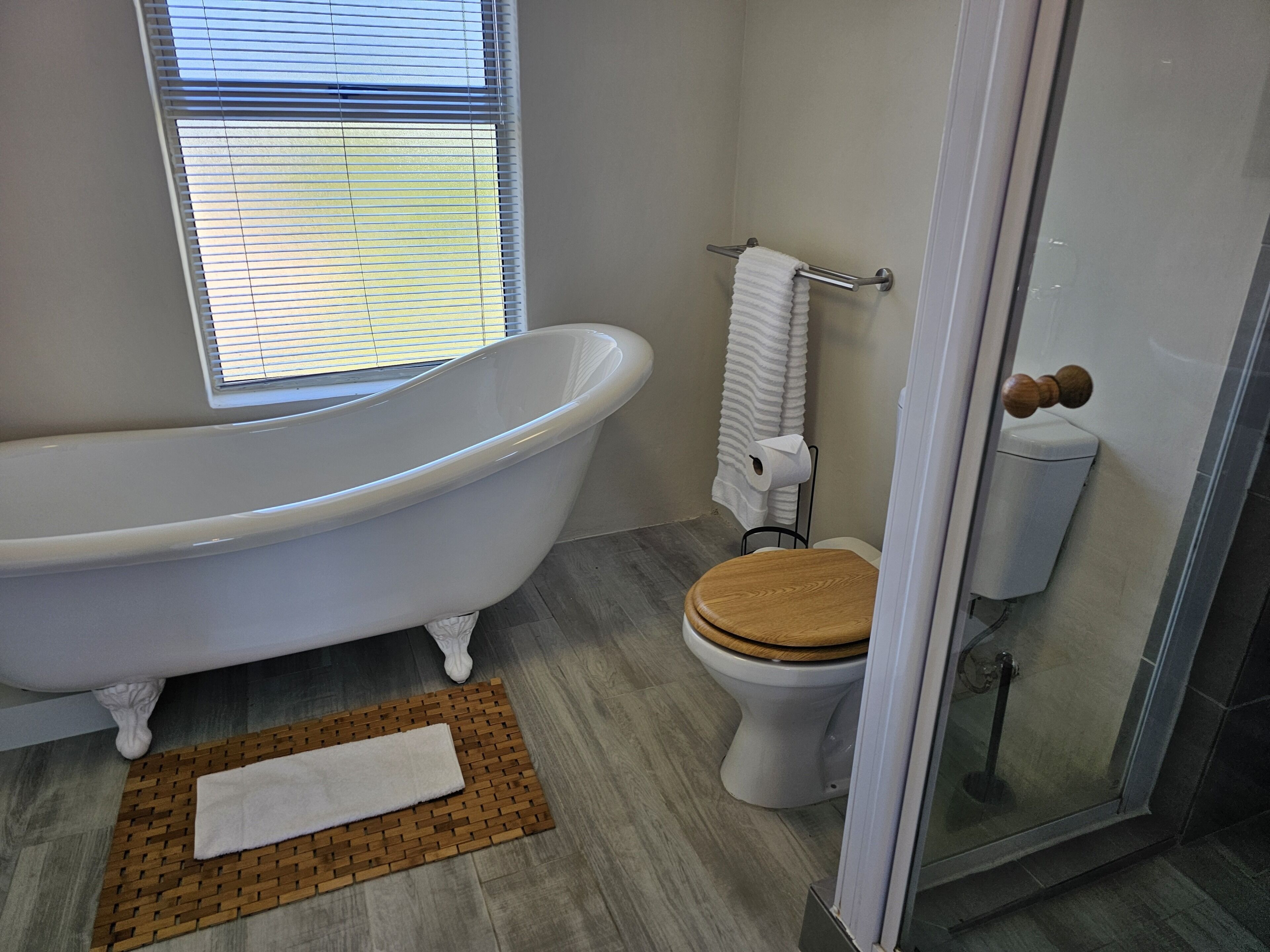 A bathroom with a freestanding bathtub, a toilet with a wooden seat, a towel rack, and a glass shower enclosure.