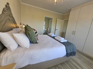 A neatly made bed with white linens and decorative pillows, a wooden headboard, and a chandelier. - Dorphene 304 by CTHA (Cape Town)
