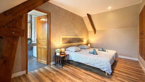 Une chambre avec une porte en bois, un lit recouvert d’une couvre-lit à motifs, une table de chevet avec une lampe et un plancher en bois.
