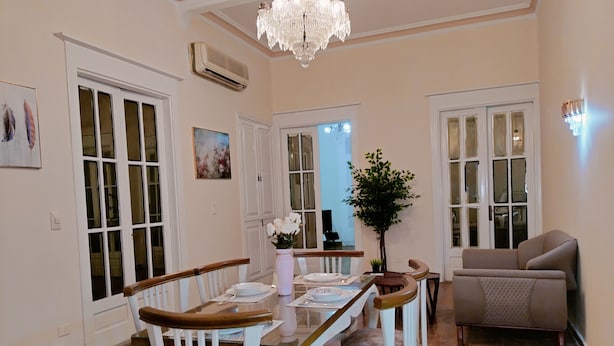 A dining area with a wooden table and white chairs, a chandelier, and a sofa in a room with wooden flooring and white walls. - Yacoubian Apartments in Downtown Cairo (Cairo)
