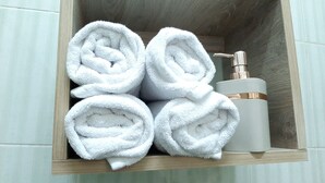 A wooden shelf with four rolled white towels and a white bottle with a pump dispenser. - Yacoubian Apartments in Downtown Cairo (Cairo)