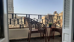 A balcony with two wicker chairs and a small table, a potted plant, and a view of buildings in the background. - Yacoubian Apartments in Downtown Cairo (Cairo)