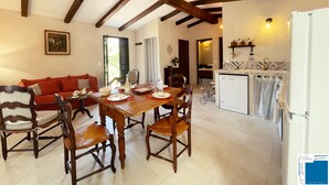 A dining area with a wooden table and chairs, a red sofa, and a kitchen with a refrigerator and sink. - Petite Bergerie Avec Piscine Privée & Climatisation (San-Gavino-Di-Carbini)