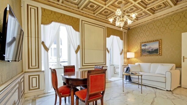 A dining area with a marble floor, a round table, and red upholstered chairs. - Elegant Apartment Near Trevi Fountain (Roma)