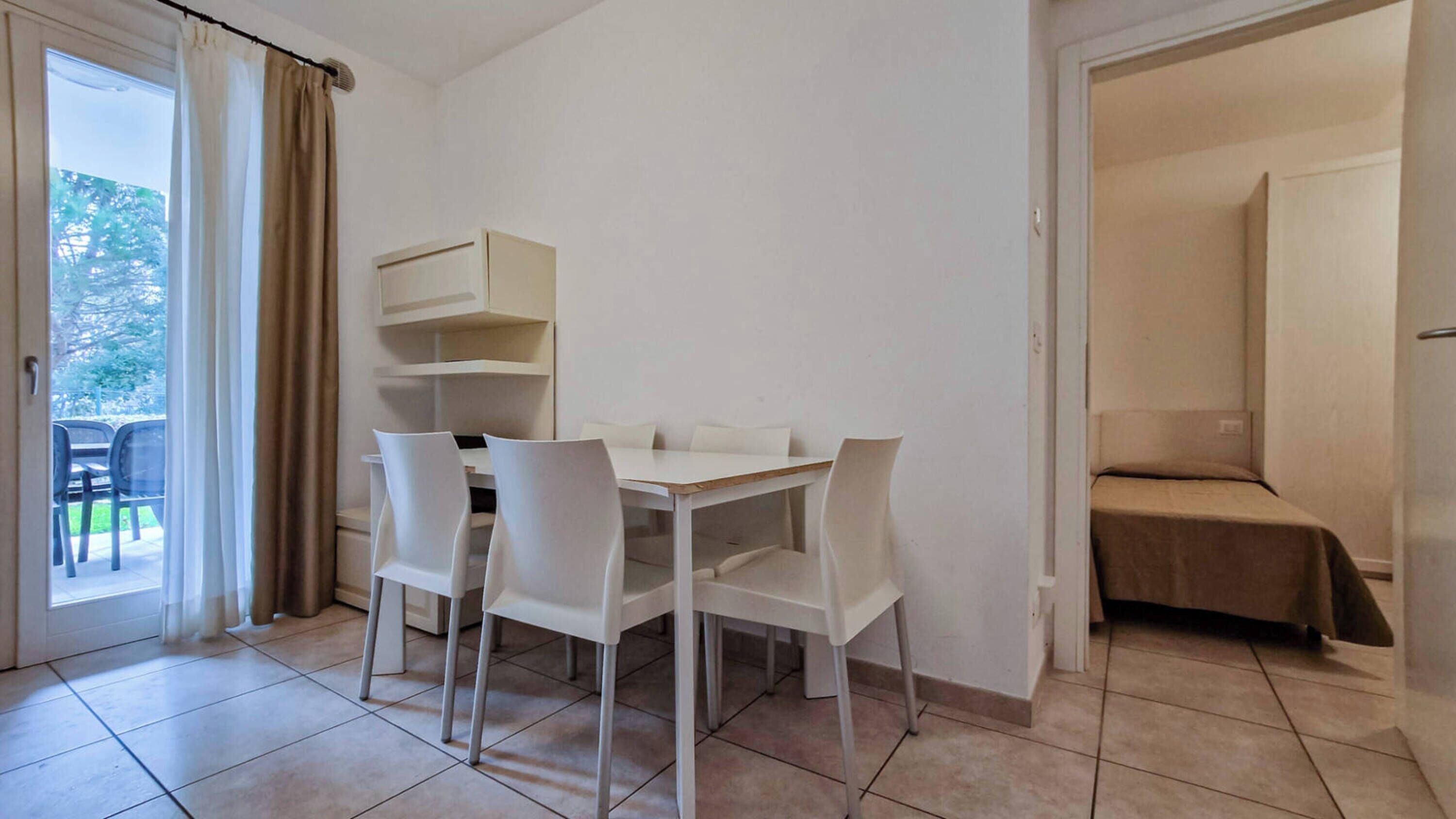 Une pièce avec une table et des chaises blanches, un petit canapé et une porte donnant sur un balcon.
