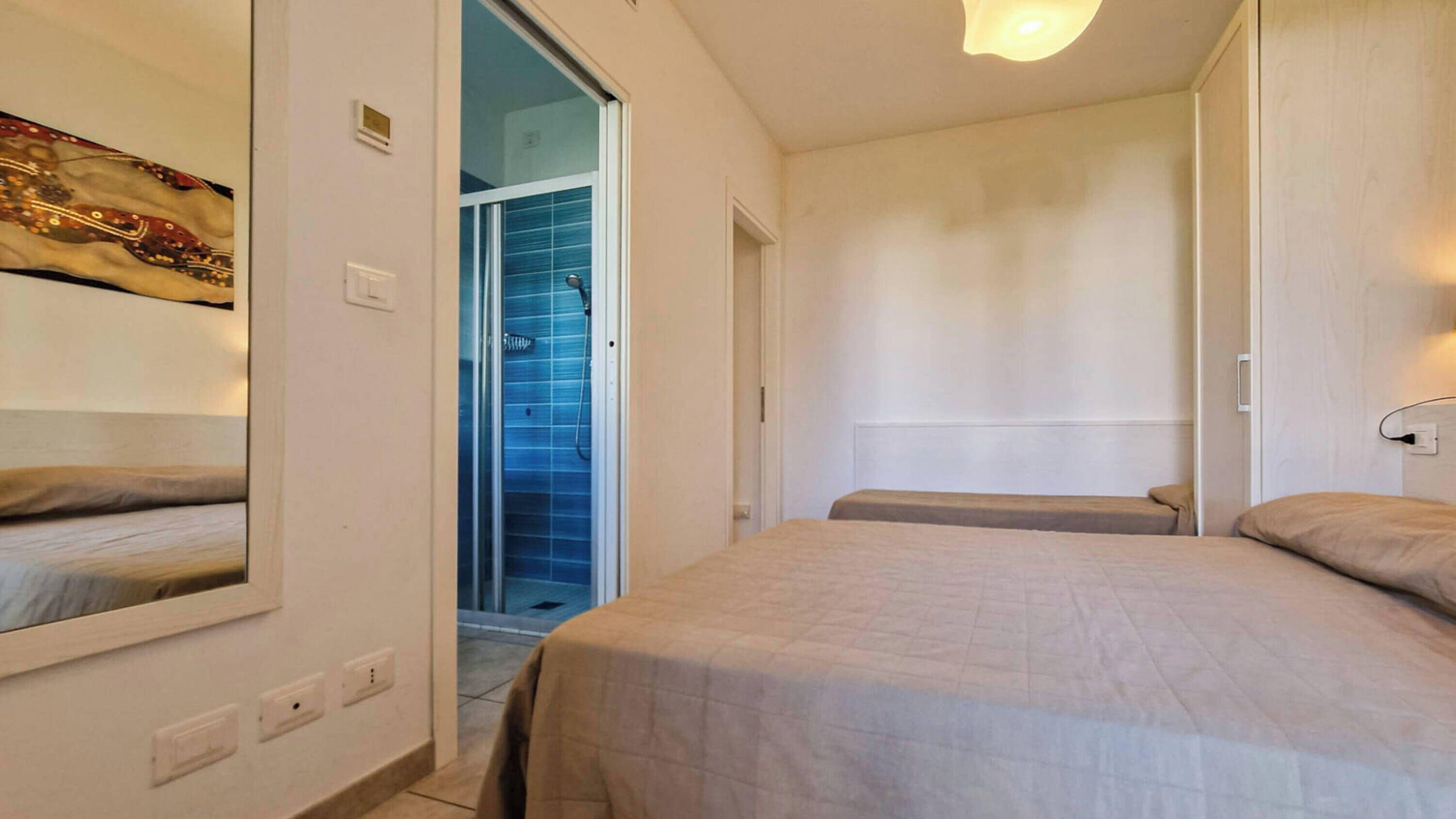 A hotel room with a bed, a shower, and a door leading to a bathroom.