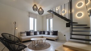 Un salon moderne avec un canapé d’angle, une table basse ronde et un fauteuil noir. On y trouve un escalier doté de panneaux éclairés et un lampadaire.