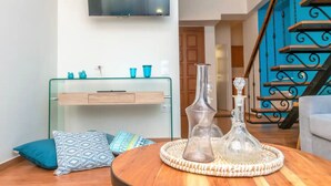 A modern living room with a glass console table, a round wooden coffee table with decorative glassware, and a staircase with a blue accent wall. - Tinos La Belle vie  (Tinos)