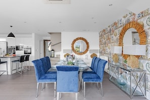 A modern dining area with a glass table, blue upholstered chairs, and a decorative wall with a circular mirror.