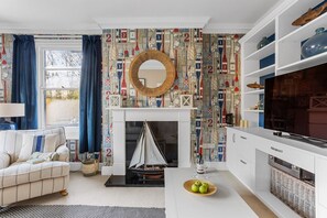 A living room with a fireplace, a sailboat model, and a patterned wallpaper.