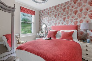 A bedroom with a bed, a nightstand, a dresser, a mirror, and a window with a view of greenery.