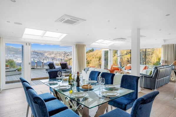 A dining area with a glass table, blue chairs, and a city view through large windows.