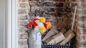 Ein Kamin mit Ziegelauskleidung, eine weiße Vase mit Blumen und ein Holzständer.