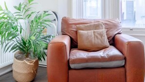 Ein Eckzimmer mit einem braunen Ledersessel, einer Topfpflanze und einem weißen Regal mit Dekoration.