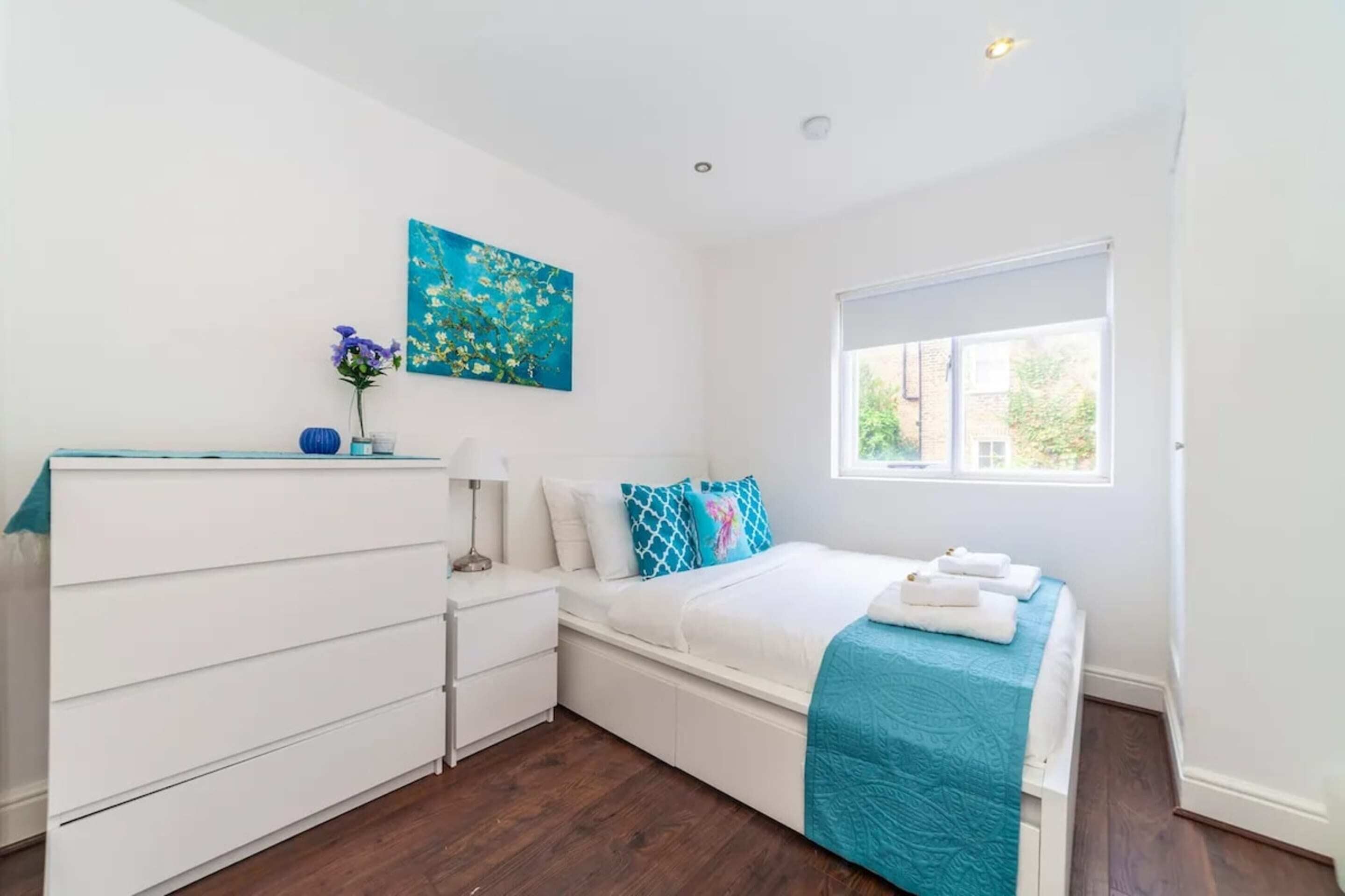 A bedroom with a bed, a dresser, a window, and a painting on the wall.