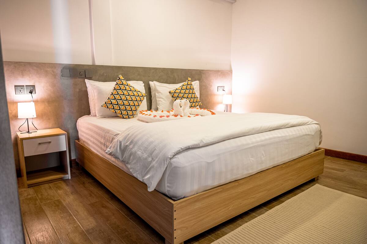 A neatly made bed with white linens, two patterned pillows, and a bedside lamp on a wooden nightstand.