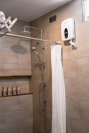Douchegedeelte met een handdouche, bedieningspaneel aan de wand en een witte douchegordijn.
