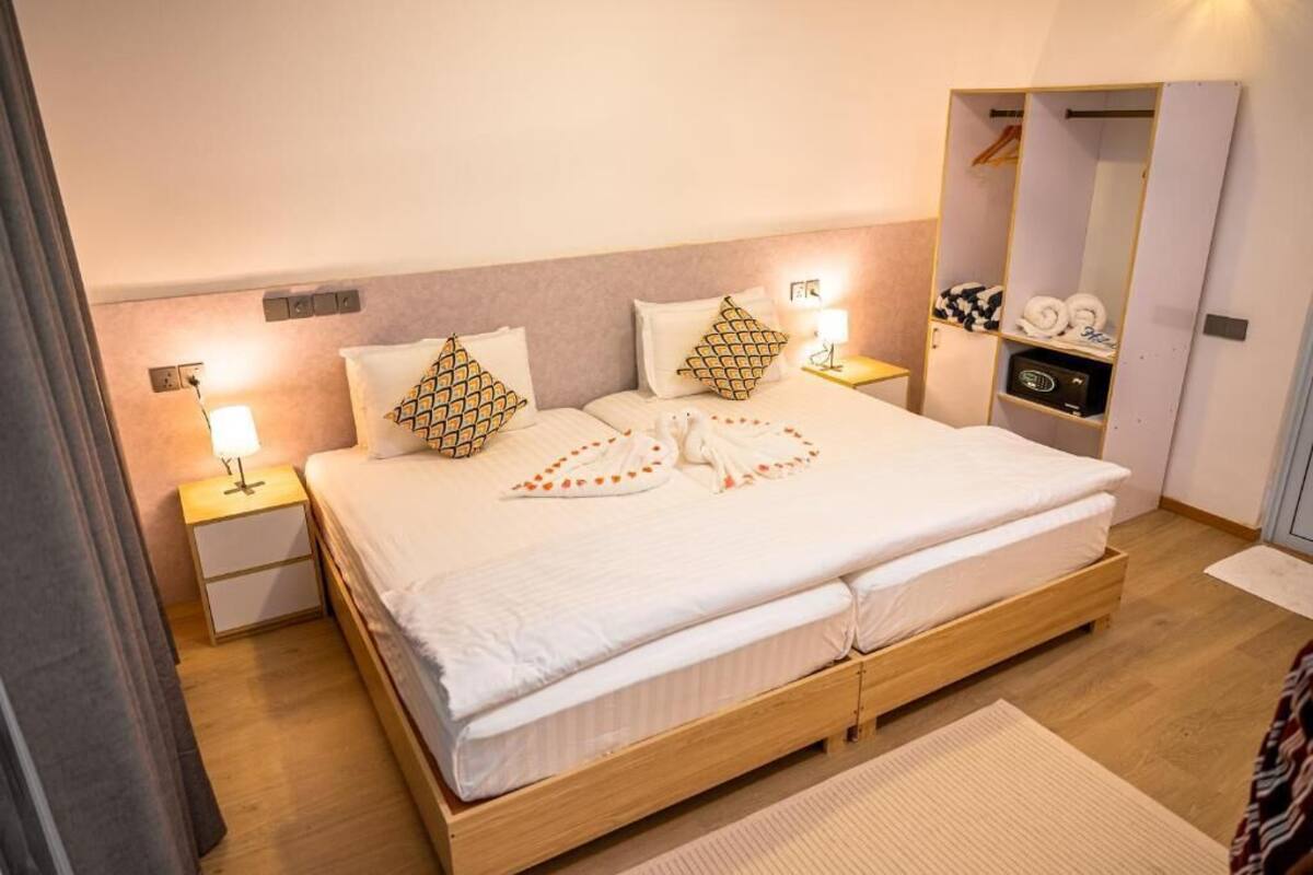 A neatly made bed with patterned pillows, a bedside lamp, a wooden nightstand, and a walk-in closet with hanging clothes.