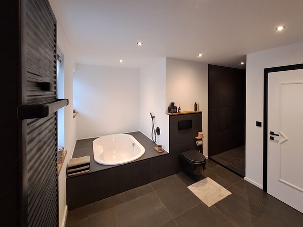 A modern bathroom with a freestanding bathtub, a toilet, and a vanity with shelves.