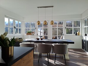 A modern kitchen with a large island, pendant lights, and a view of the outdoors through large windows.