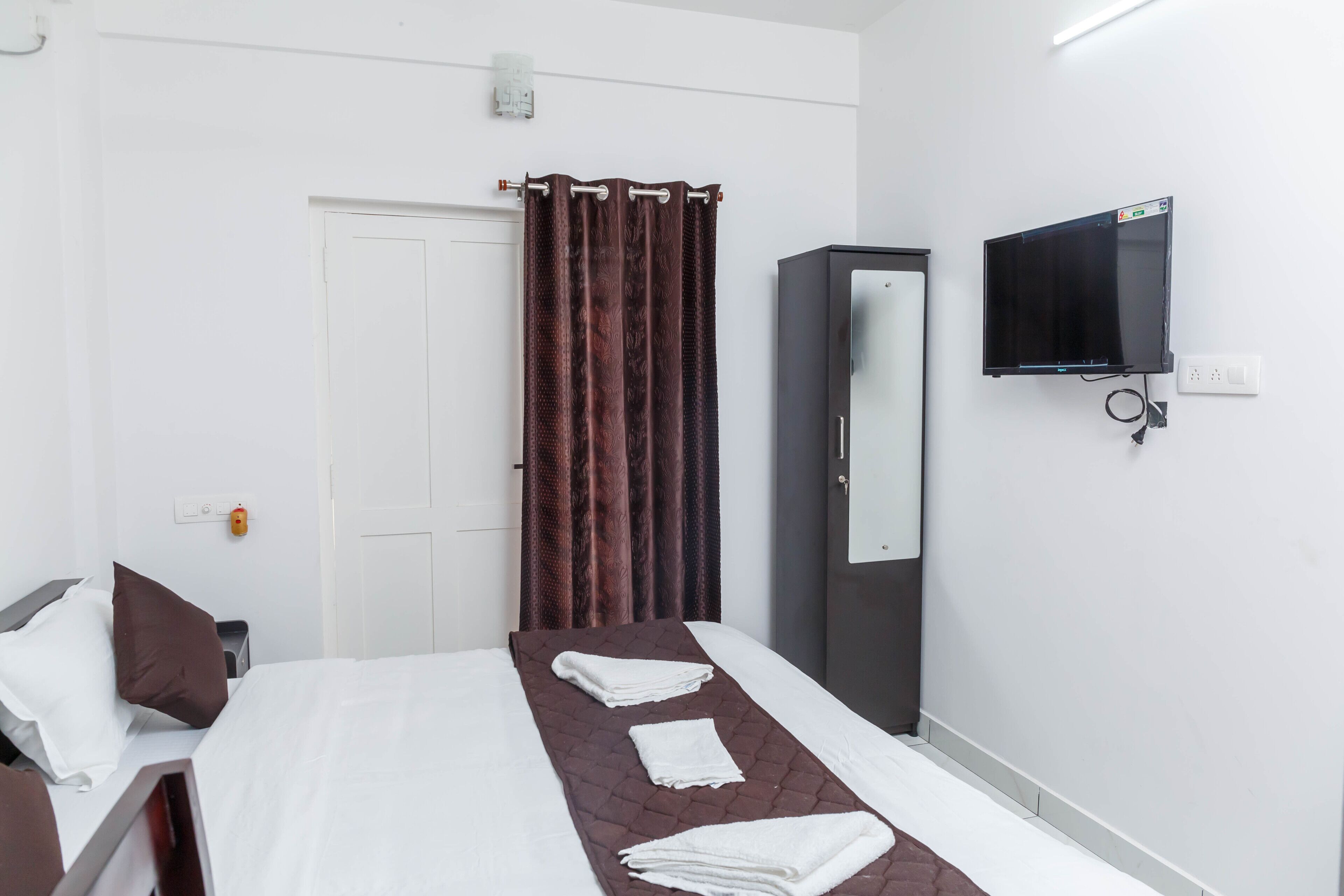 A hotel room with a bed, a TV mounted on the wall, a wardrobe, and a curtain.