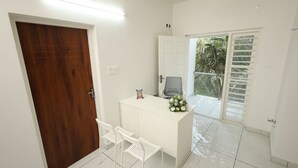 A room with a white desk, two white chairs, a wooden door, and a white wall. - Guest West Inn (Kanayannur)