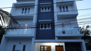 A modern two-story building with a flat roof, a central entrance with a wooden door, and a checkered floor pattern. - Guest West Inn (Kanayannur)