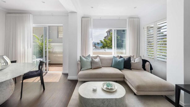 Un salón moderno con un sofá beige, una mesa de centro de mármol y vistas a un balcón con plantas.