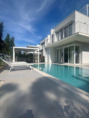 A modern house with a swimming pool, outdoor seating, and a covered patio area. - Stunning Villa With Pool and Lagoon View (Rosolina)