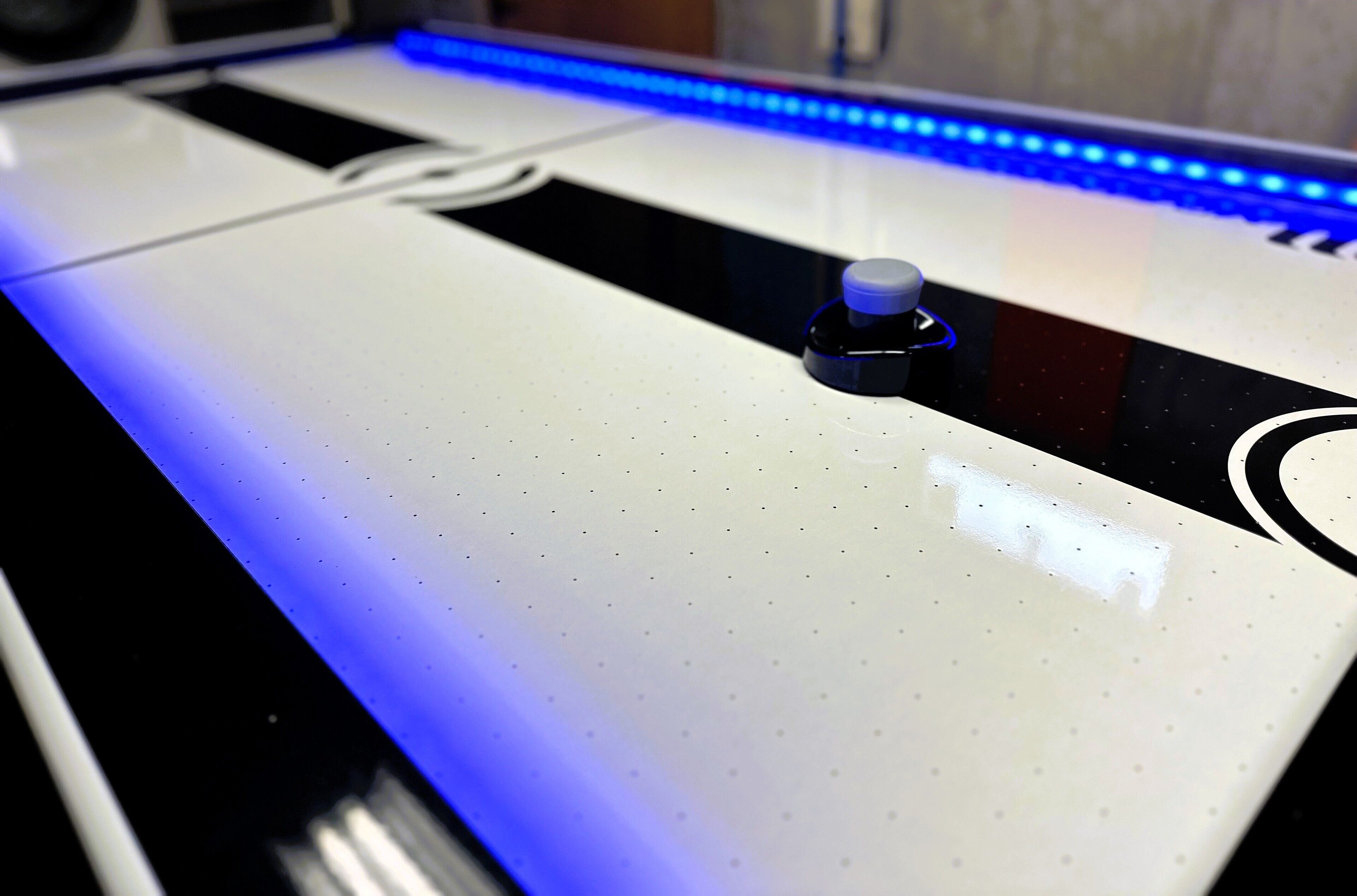 Una mesa blanca con una tira LED azul y un pequeño objeto negro encima.