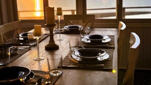Une table à manger dressée pour deux personnes, avec assiettes, verres et une bougie, offrant une vue sur le coucher du soleil.
