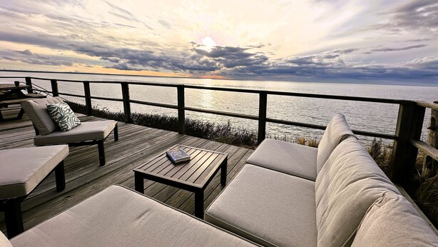 Une terrasse avec des sièges extérieurs et une vue sur l’océan au coucher du soleil.