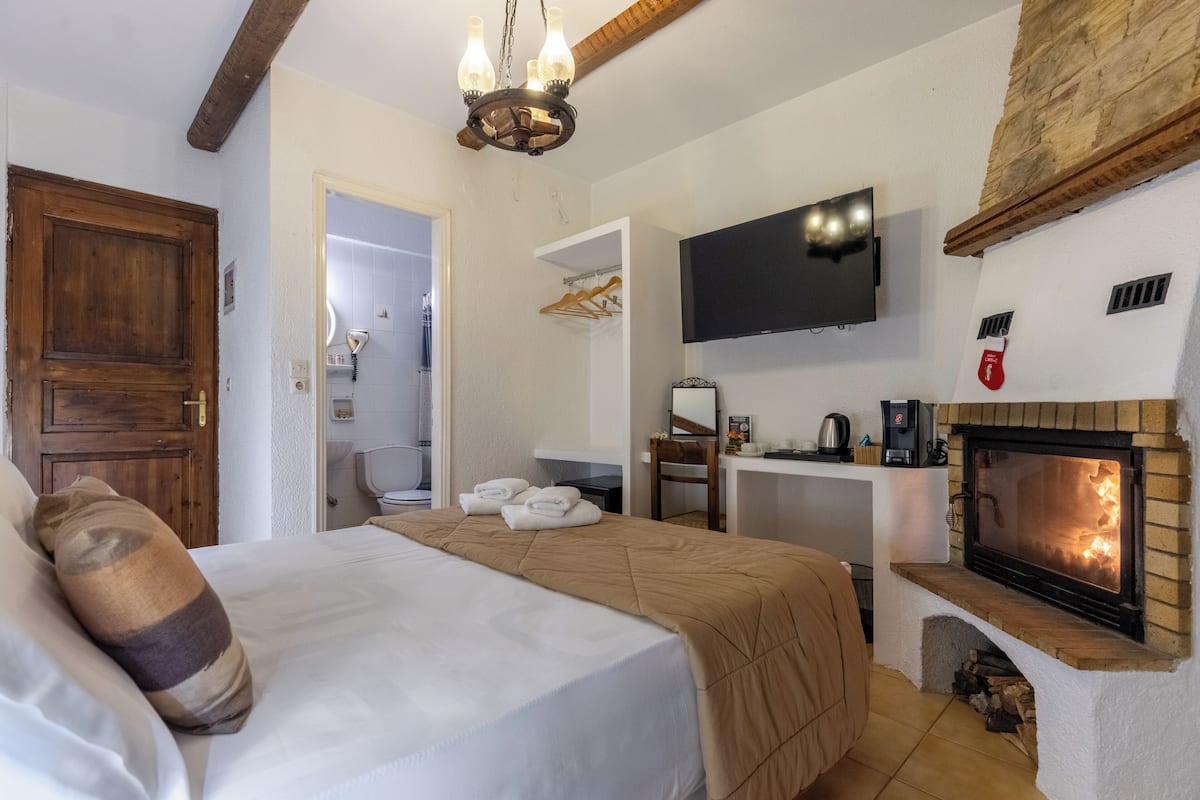 A bedroom with a bed, a television, a fireplace, and a wooden ceiling beam.