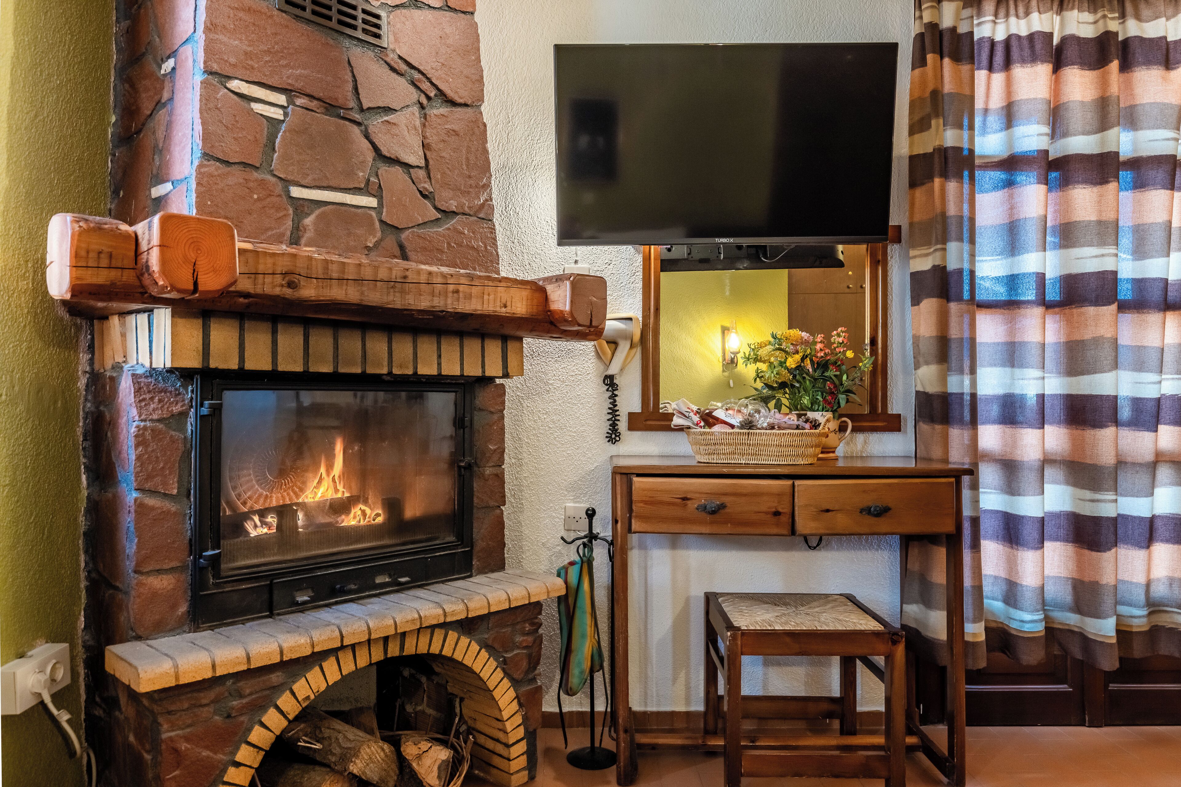 A stone fireplace with a TV above it, a small wooden table, and a striped curtain.