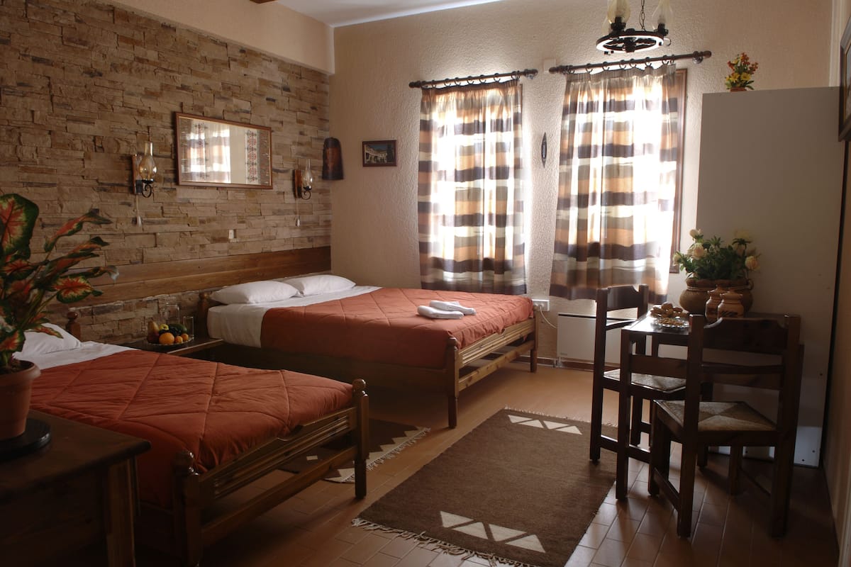 A room with two beds, a wooden desk, a chair, a potted plant, and a brick wall.
