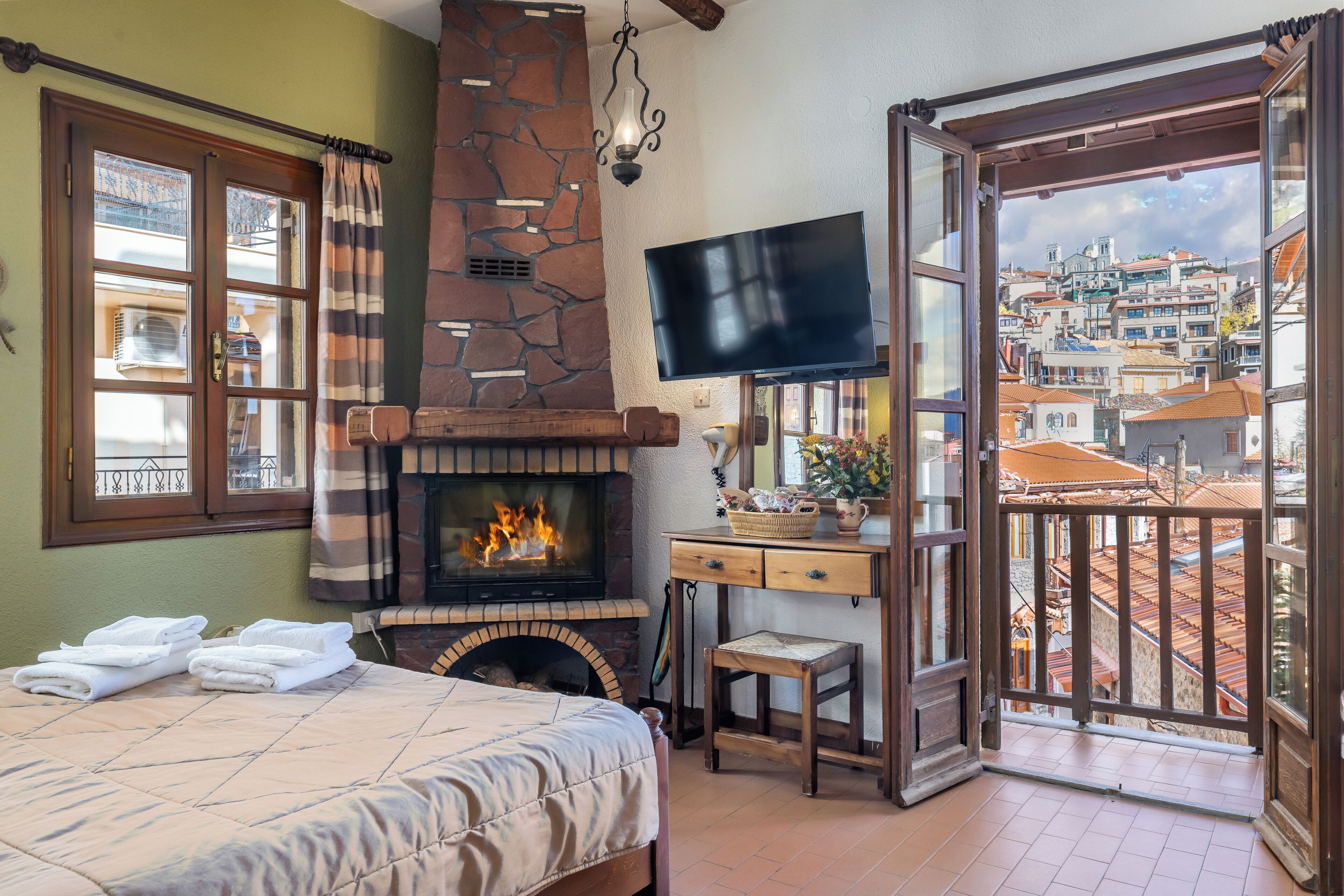 Una habitación con chimenea, cama, televisor y balcón con vistas a la ciudad.