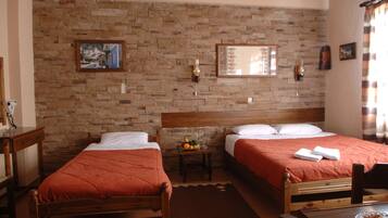 Habitación de hotel con dos camas de madera, una pared de ladrillo, una mesita con fruta y una silla de madera.