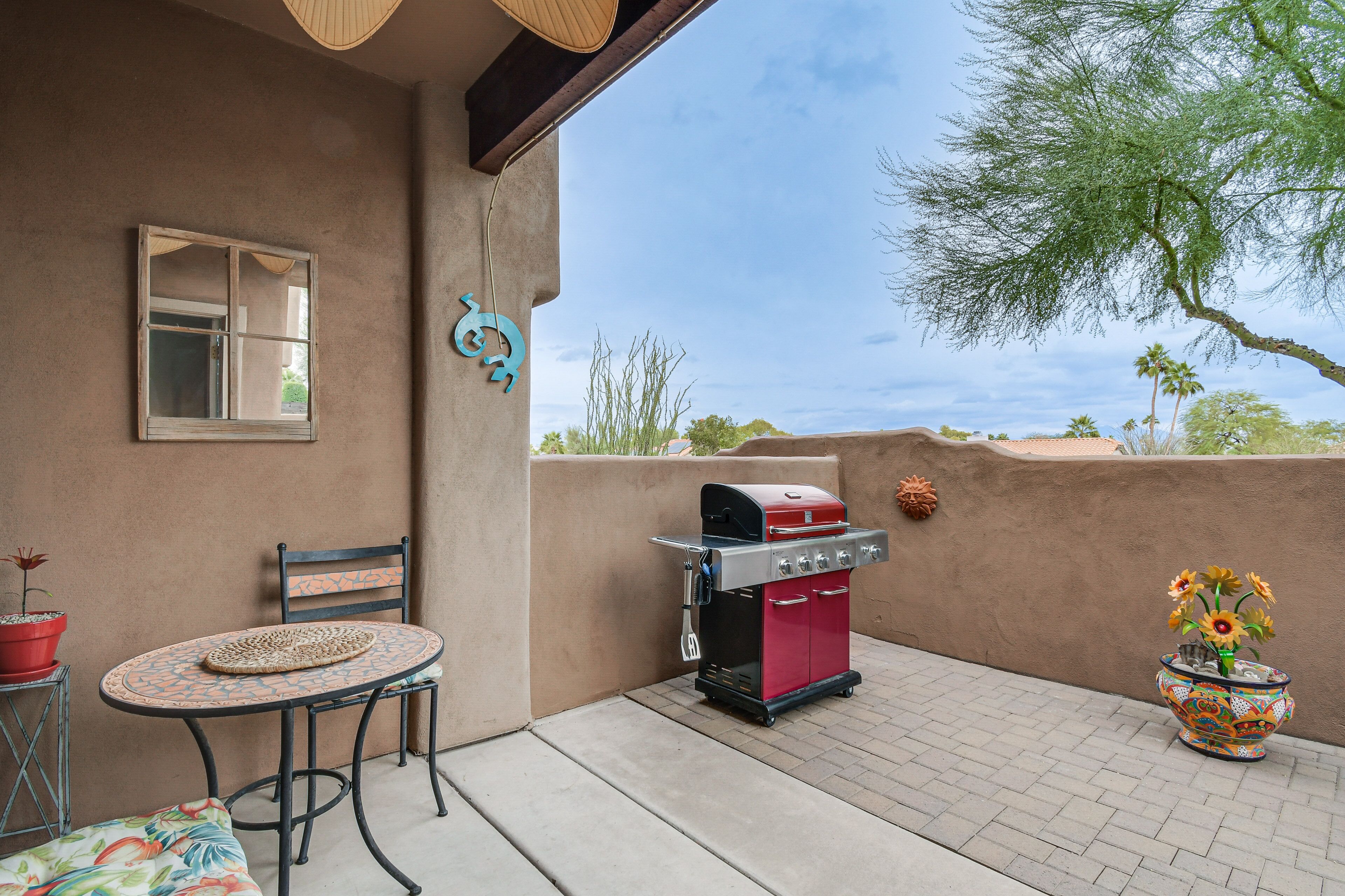 An outdoor patio with a round table, a grill, and a potted plant.