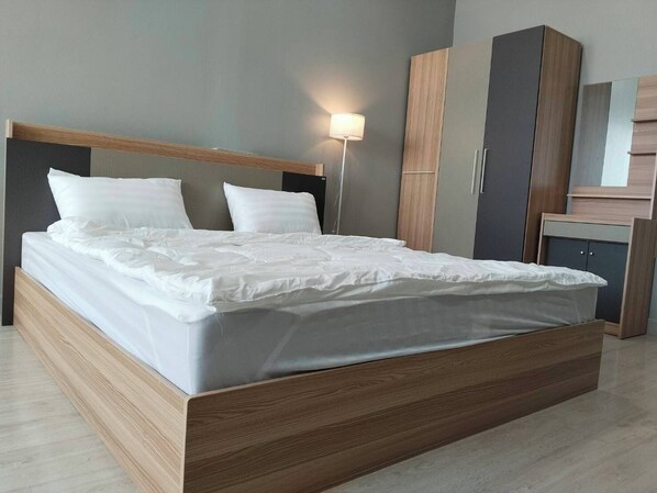 Ein modernes Schlafzimmer mit einem Bettgestell aus Holz, weißer Bettwäsche und einem grauen Kopfteil.