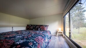 A bedroom with a large bed, a small bedside table, a window with a view of greenery, and built-in cabinets.