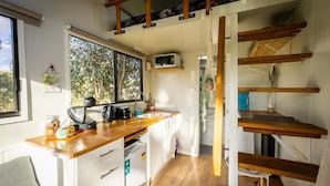 A compact kitchen with a wooden countertop, white cabinets, a microwave, and a window with a view of trees.