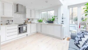 A modern kitchen with white cabinets, a built-in oven, and a large window. - Beautifully Designed 2BD House - by Queen's Park! (London)