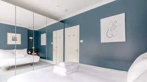 A modern bedroom with a large bed, a wardrobe, and a mirror. - Beautifully Designed 2BD House - by Queen's Park! (London)