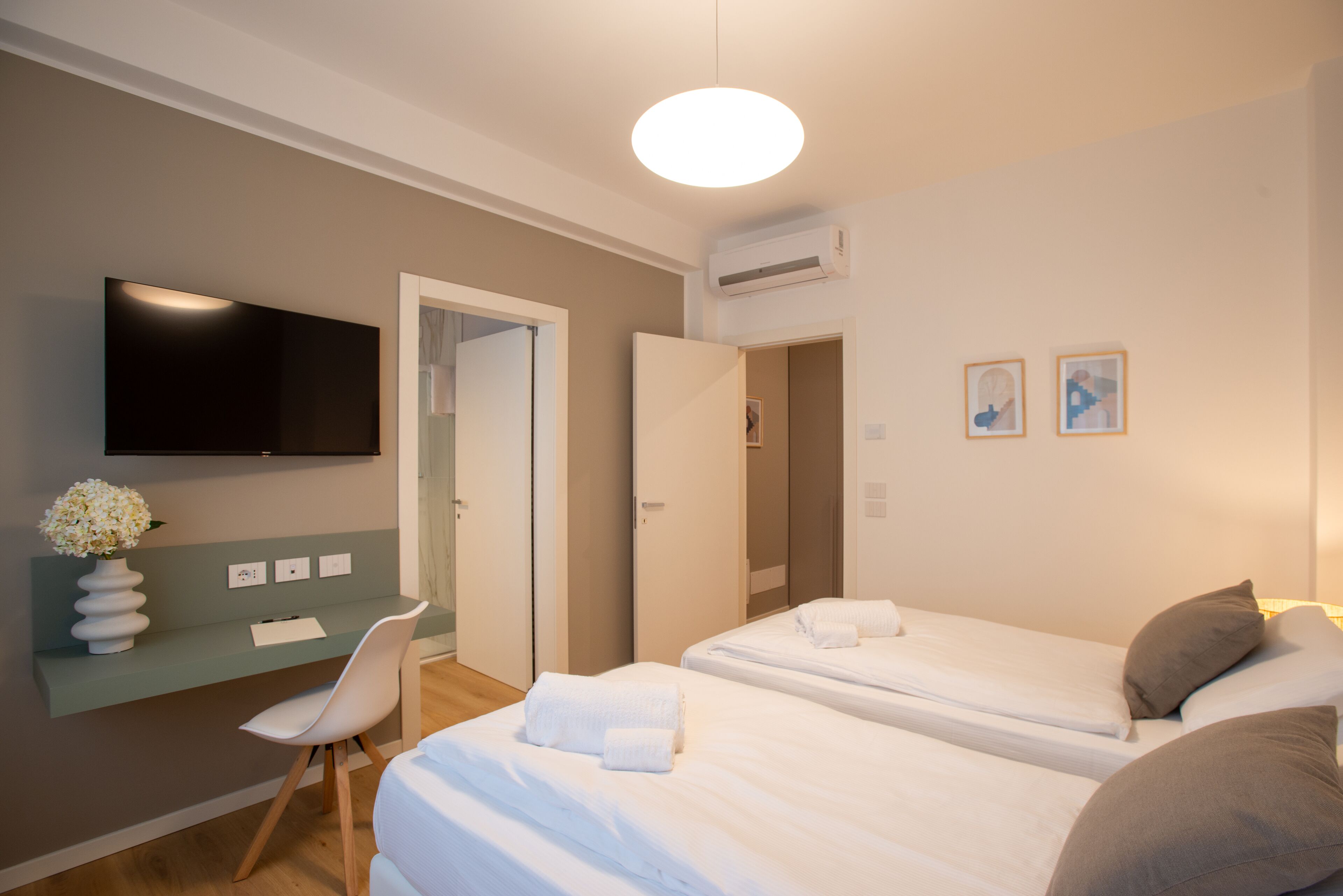 Habitación de hotel con escritorio, silla, dos camas, televisor de pantalla plana y una obra de arte en la pared.
