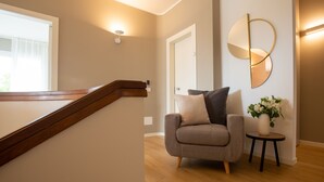 A modern interior with a wooden staircase, a grey sofa, a round mirror, and a small table with a vase of flowers.